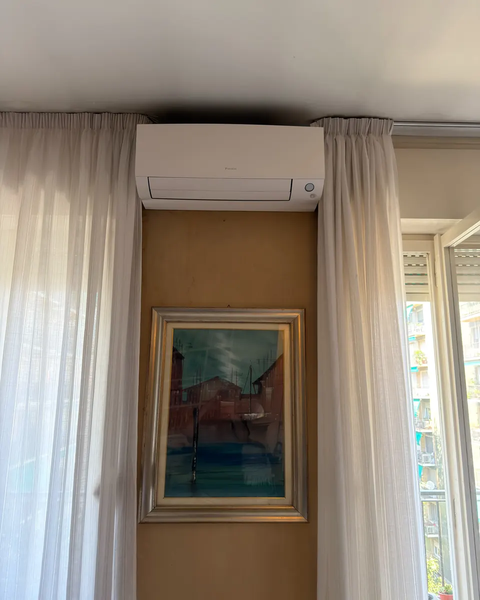 Split Daikin Perfera sopra un quadro, tra le tende
